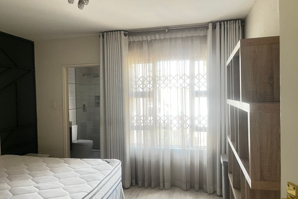 A bedroom featuring laminate flooring, a security gate on the window, and direct access to an en-suite bathroom.
