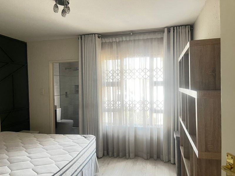 A bedroom featuring laminate flooring, a security gate on the window, and direct access to an en-suite bathroom.