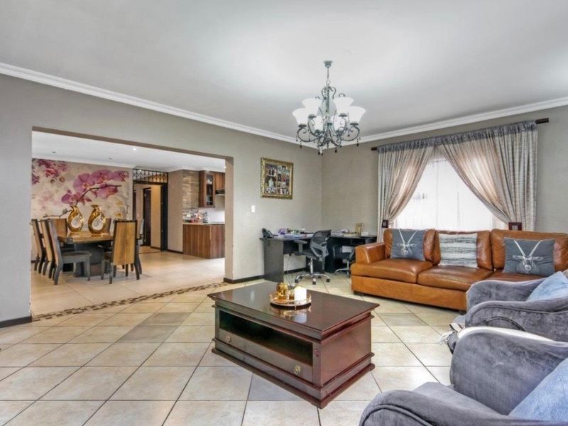 Spacious open-plan living and dining area featuring tiled floors, crown molding, and a central chandelier, seamlessly connecting to the kitchen space.