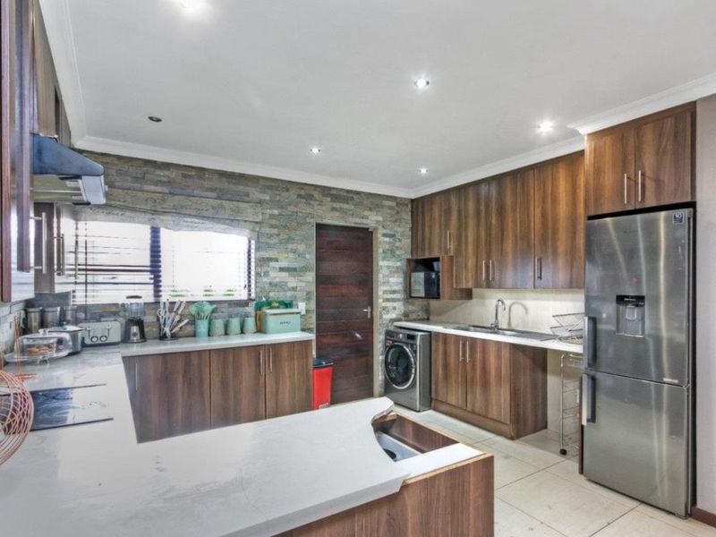 Modern kitchen featuring dark wood cabinetry, stone veneer accent wall, quartz countertops, and integrated appliances with recessed lighting.