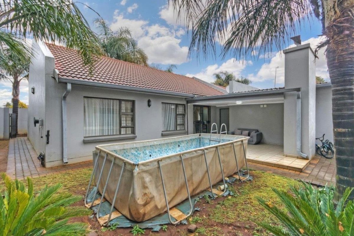 Rear view of the property featuring a covered patio, tiled roof, and a paved garden area with an above-ground pool.