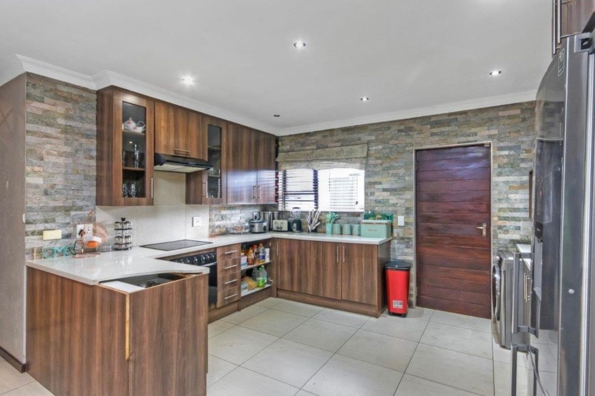 A modern kitchen featuring wood-finish cabinetry, stone veneer accent walls, stone countertops, and integrated appliances with recessed lighting.