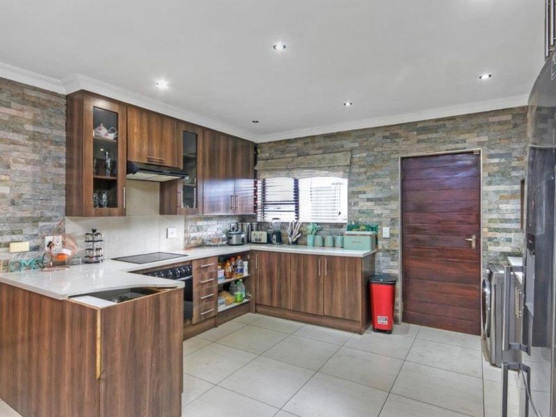 A modern kitchen featuring wood-finish cabinetry, stone veneer accent walls, stone countertops, and integrated appliances with recessed lighting.