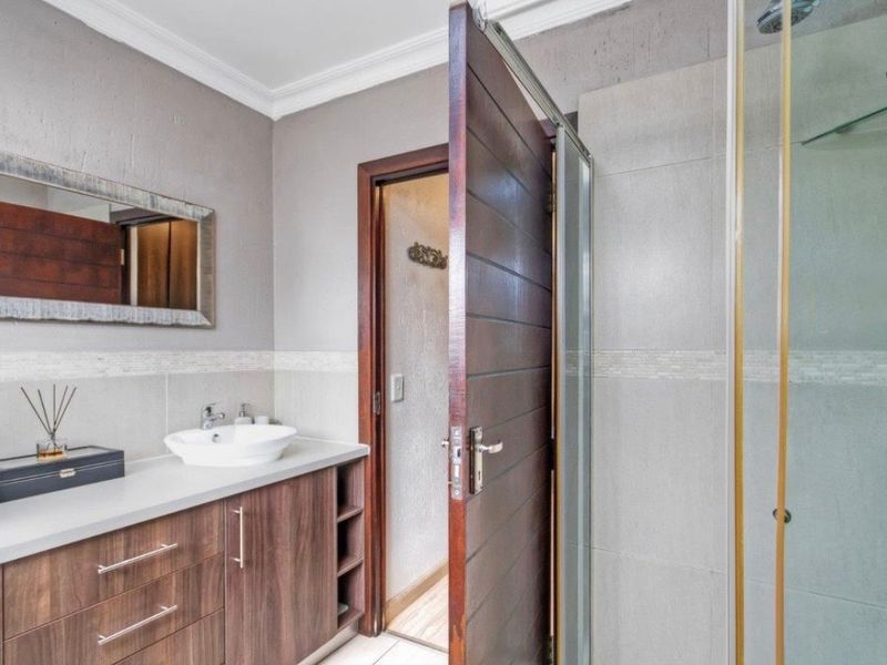 Modern bathroom featuring a vanity cabinet with a countertop basin, tiled walls, and a glass-enclosed shower.