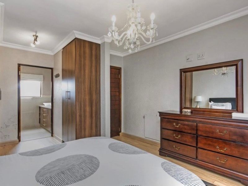 Spacious bedroom featuring built-in cupboards, crown molding, and direct access to an en-suite bathroom with laminate flooring throughout.