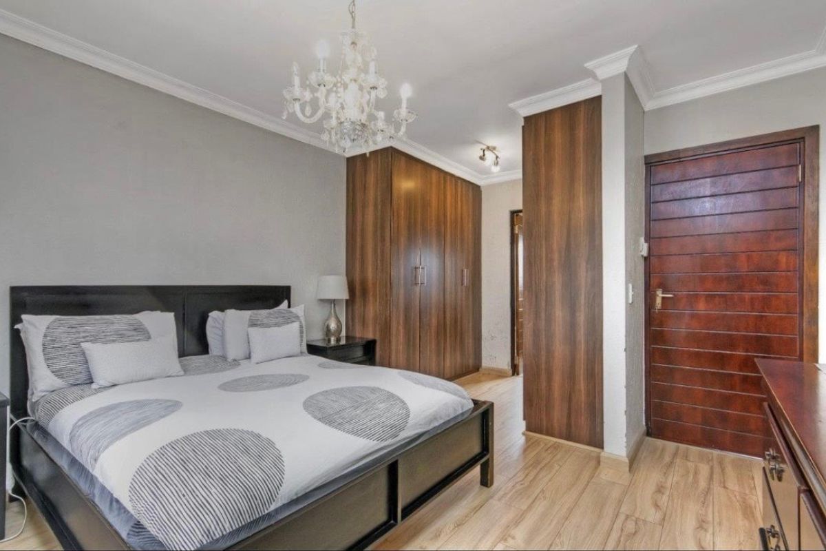 A well-maintained bedroom featuring built-in wooden cupboards, laminate flooring, crown molding, and a classic chandelier, offering a clean and functional living space.