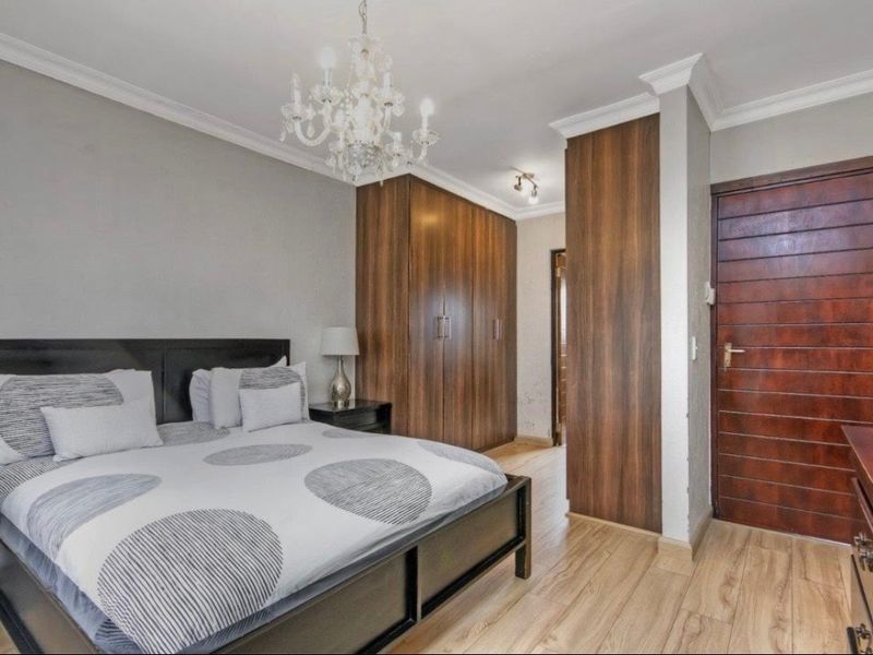 A well-maintained bedroom featuring built-in wooden cupboards, laminate flooring, crown molding, and a classic chandelier, offering a clean and functional living space.