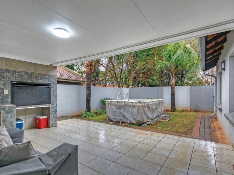 Covered patio area featuring a built-in braai, tiled flooring, and direct access to the rear garden and pool area.