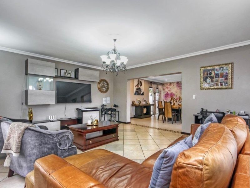 Spacious open-plan living and dining area featuring tiled flooring, decorative cove cornicing, and a central chandelier, creating a comfortable and connected living space.