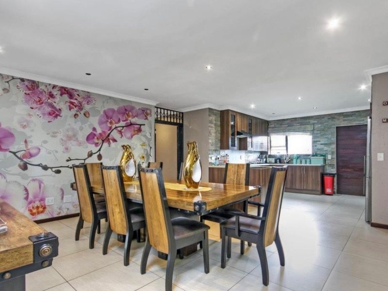 Spacious open-plan dining and kitchen area featuring tiled floors, recessed lighting, a stone-clad kitchen backsplash, and a decorative floral feature wall.
