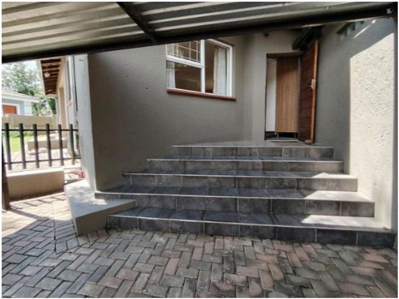 Front entrance area featuring tiled steps leading to a timber door, complemented by a paved driveway and a metal carport structure.