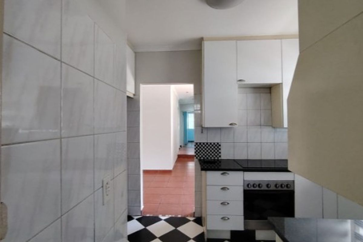 A functional kitchen featuring white cabinetry, black stone countertops, a built-in oven, and a classic black-and-white checkered tiled floor.