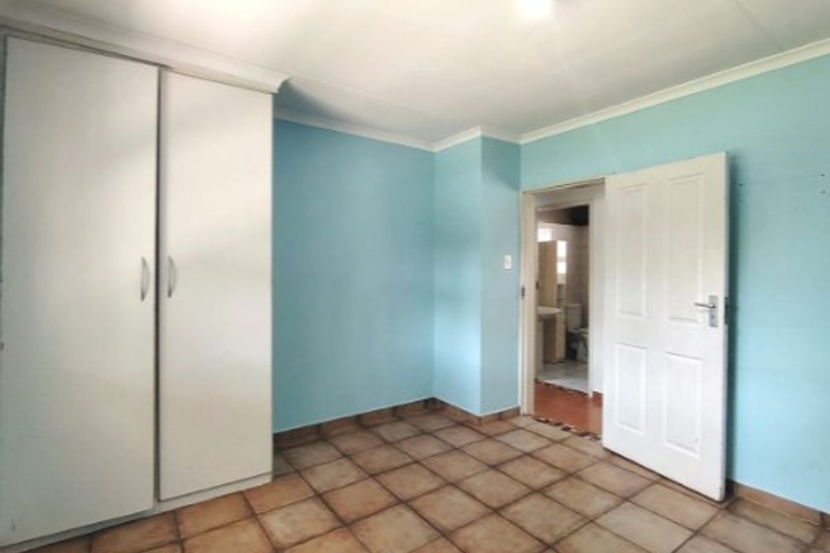 A vacant bedroom featuring built-in cupboards, tiled flooring, and direct access to an adjoining bathroom.