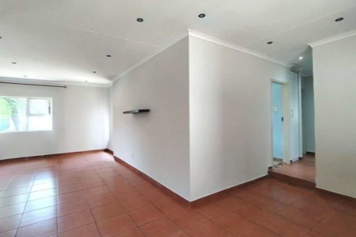 An empty, open-plan living area featuring neutral walls, ceramic tiled flooring, and recessed downlighting throughout the space.