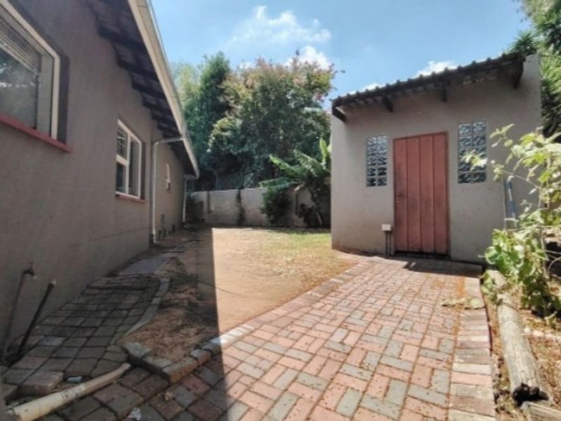 Rear garden area featuring brick paved pathways, a detached outbuilding with glass block accents, and a perimeter boundary wall.