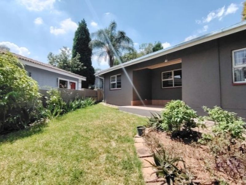 A well-maintained rear exterior view featuring a covered patio, landscaped garden, and boundary wall with modern aluminium window frames.