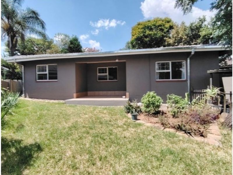 Rear view of the house featuring a covered patio, well-maintained garden, and modern aluminium window frames.