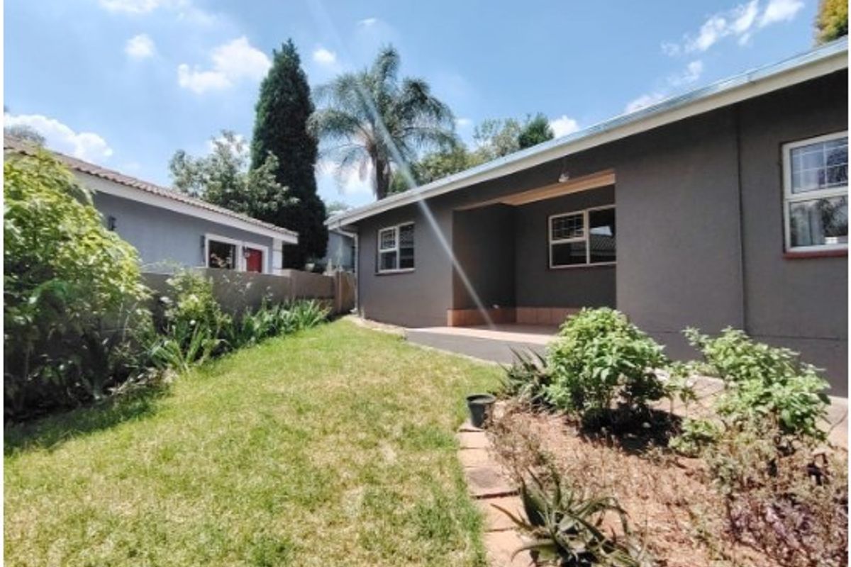 A view of the rear exterior featuring a covered patio area, landscaped garden, and perimeter walling.