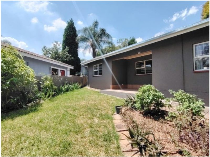 A view of the rear exterior featuring a covered patio area, landscaped garden, and perimeter walling.