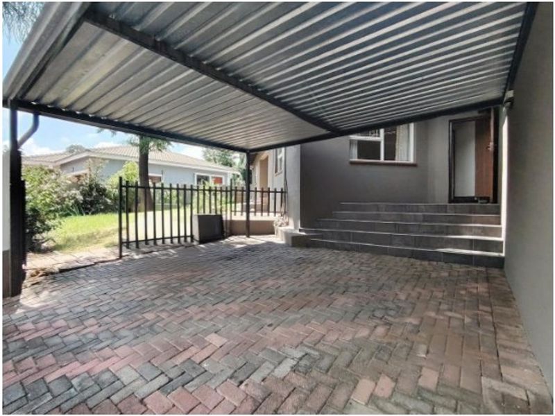 A covered carport area featuring a corrugated metal roof, brick paving, and tiled steps leading to the main entrance of the house.