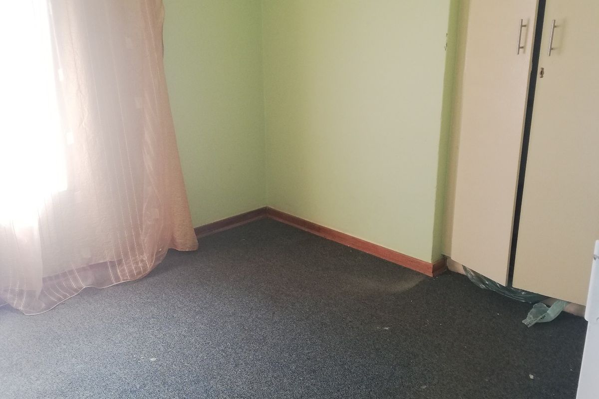 A vacant bedroom featuring built-in wardrobe storage, carpeted flooring, and light green wall paint, offering a blank canvas for potential updates.