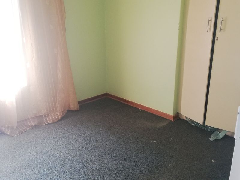 A vacant bedroom featuring built-in wardrobe storage, carpeted flooring, and light green wall paint, offering a blank canvas for potential updates.