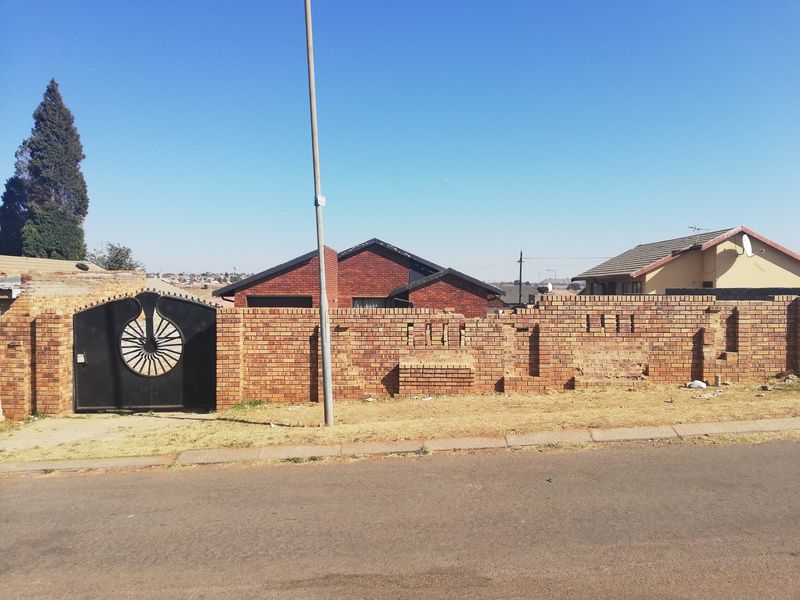 Front view of the property featuring a brick boundary wall and a decorative metal pedestrian gate, showing signs of wear and maintenance requirements.