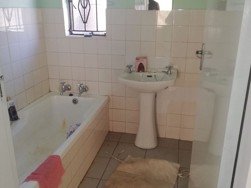 A dated bathroom featuring a pedestal basin, built-in bathtub, and tiled finishes, requiring cosmetic updates to modernize the space.