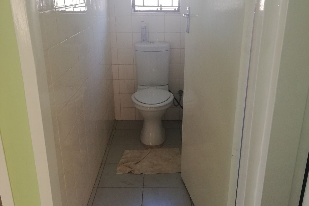 A compact, functional guest toilet featuring tiled walls and flooring, equipped with a standard toilet suite and a security-fitted window.