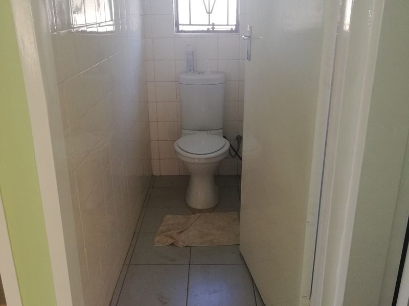 A compact, functional guest toilet featuring tiled walls and flooring, equipped with a standard toilet suite and a security-fitted window.