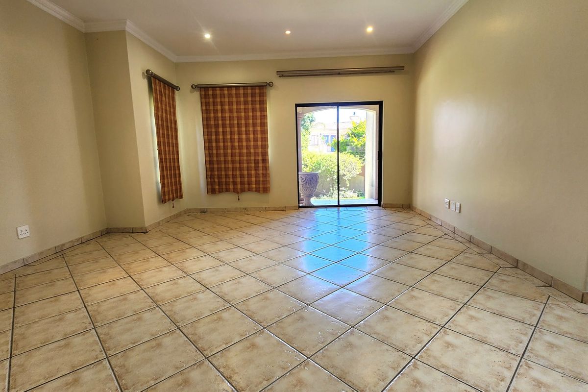 A spacious, empty living room featuring neutral walls, tiled flooring, and a sliding glass door providing access to the outdoor area.
