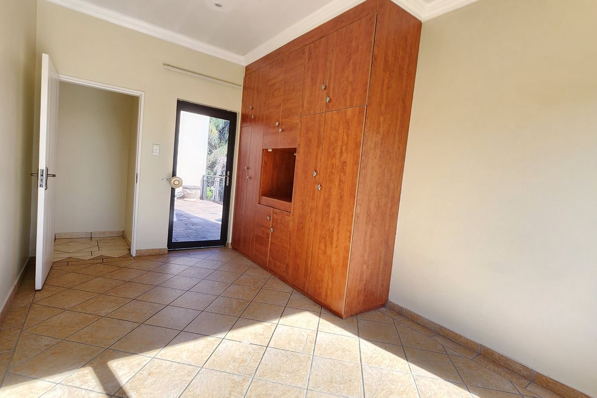 A bright, empty bedroom featuring built-in wooden cupboards, tiled flooring, and direct access to an outdoor patio area.