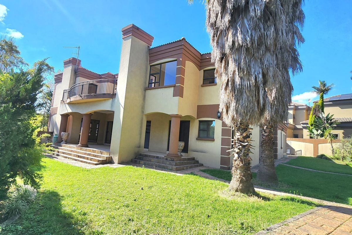 Rear view of a multi-story house featuring a balcony, stone steps, and a landscaped garden area.