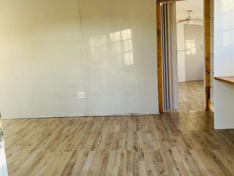 An empty living area featuring laminate wood-look flooring, a vaulted ceiling, and a folding door leading to an adjacent room.