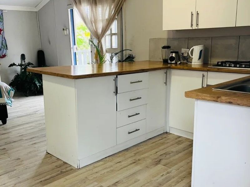 Open plan kitchen area featuring white cabinetry, wooden countertops, gas hob, and light-toned laminate flooring, seamlessly connecting to the adjacent living space.