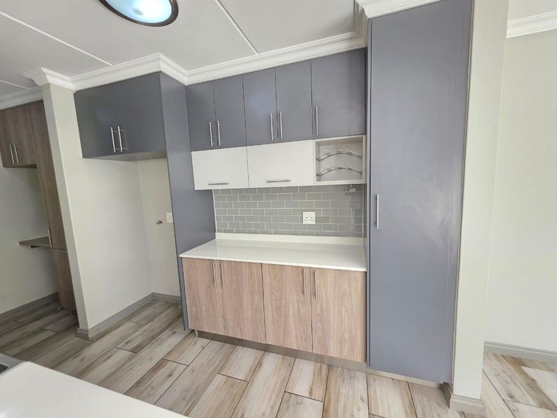 Modern kitchen featuring two-tone cabinetry, subway tile backsplash, stone countertops, and wood-look tile flooring with ample storage space.