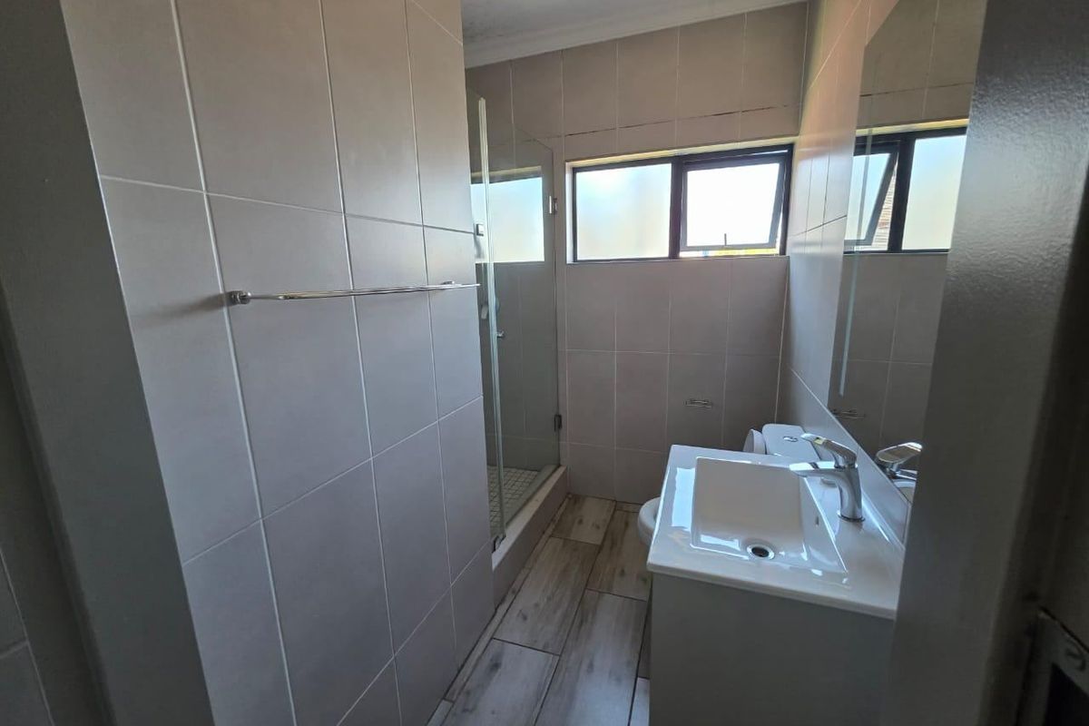 A functional bathroom featuring a shower enclosure, vanity basin, toilet, and neutral wall and floor tiling.