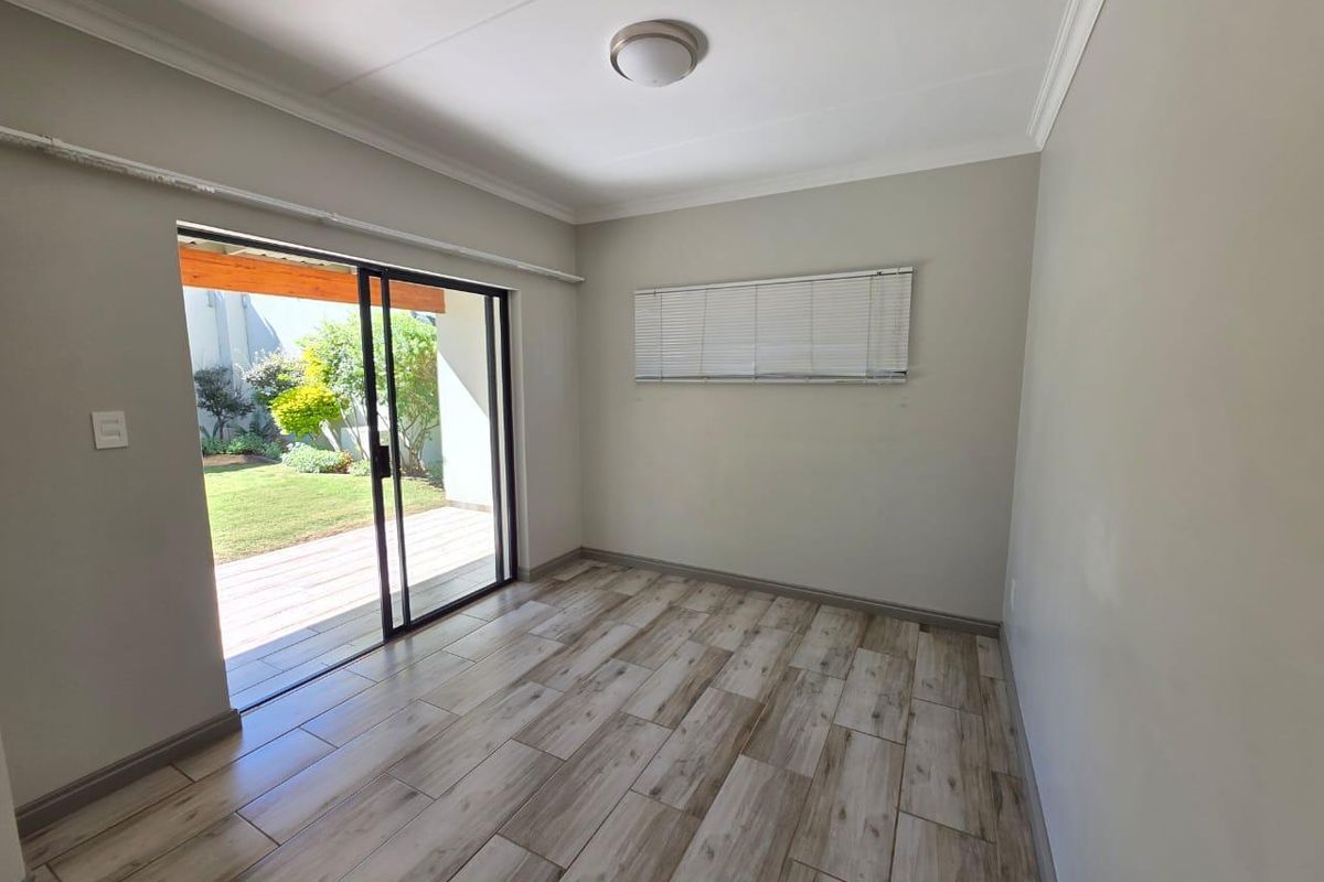 A bright, empty bedroom featuring wood-look tile flooring, a ceiling light, and a sliding glass door providing direct access to the garden patio.