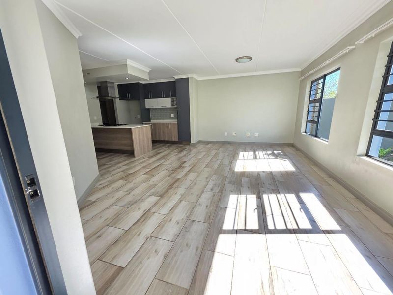 Spacious open-plan living area featuring modern wood-look tile flooring, a contemporary kitchen with built-in cabinetry, and large windows with security bars.
