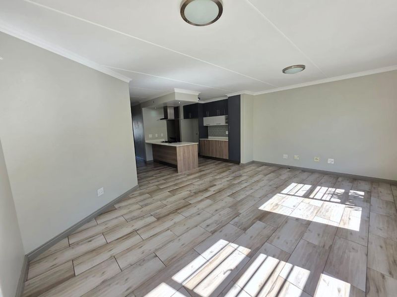 Spacious open-plan living area featuring modern wood-look tile flooring and a contemporary kitchen with built-in cabinetry, island, and extractor fan.