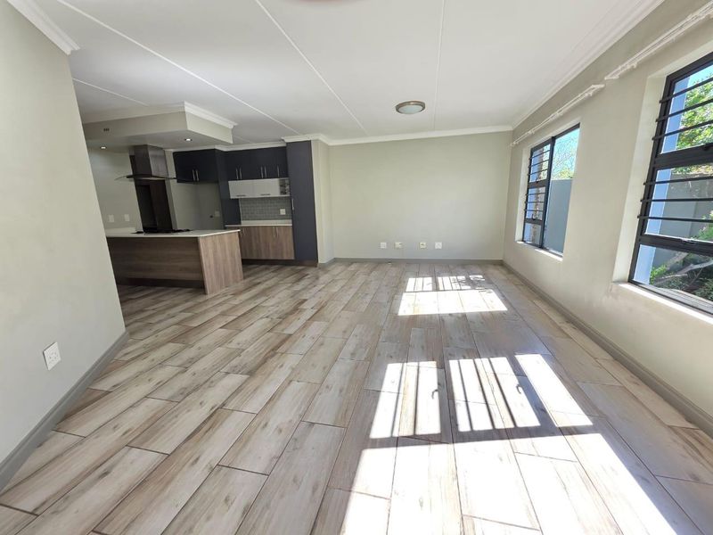 Spacious open-plan living area featuring modern tiled flooring, a contemporary kitchen with built-in cabinetry, and large windows with security bars.