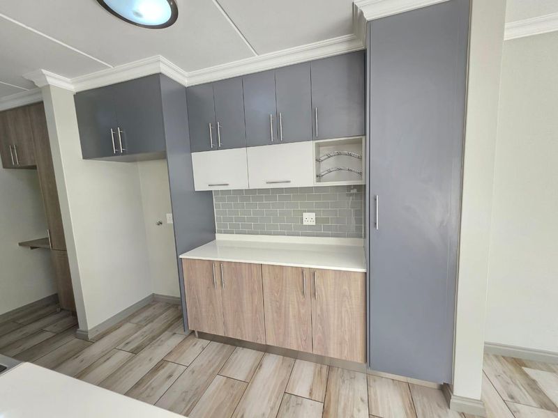 Modern kitchen featuring two-tone cabinetry, subway tile backsplash, stone countertops, and wood-look tile flooring in a clean, well-maintained space.