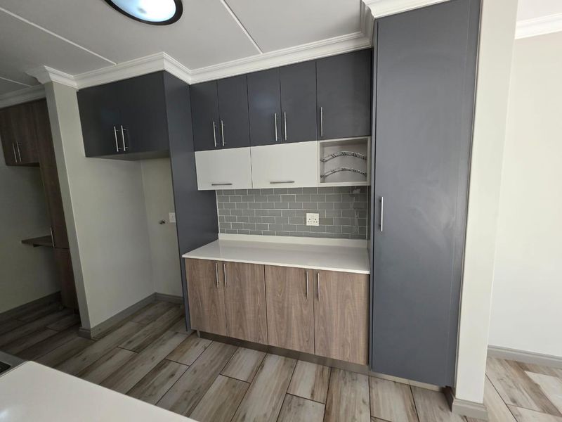 Modern kitchen featuring two-tone cabinetry, subway tile backsplash, stone countertops, and ample storage space with a tall pantry cupboard.