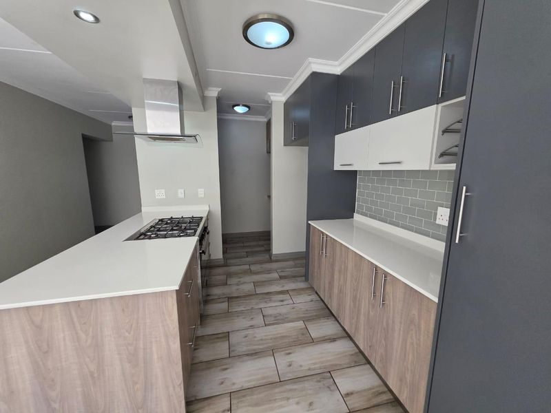Modern kitchen featuring two-tone cabinetry, quartz countertops, a gas hob with extractor fan, subway tile backsplash, and durable wood-look tile flooring.