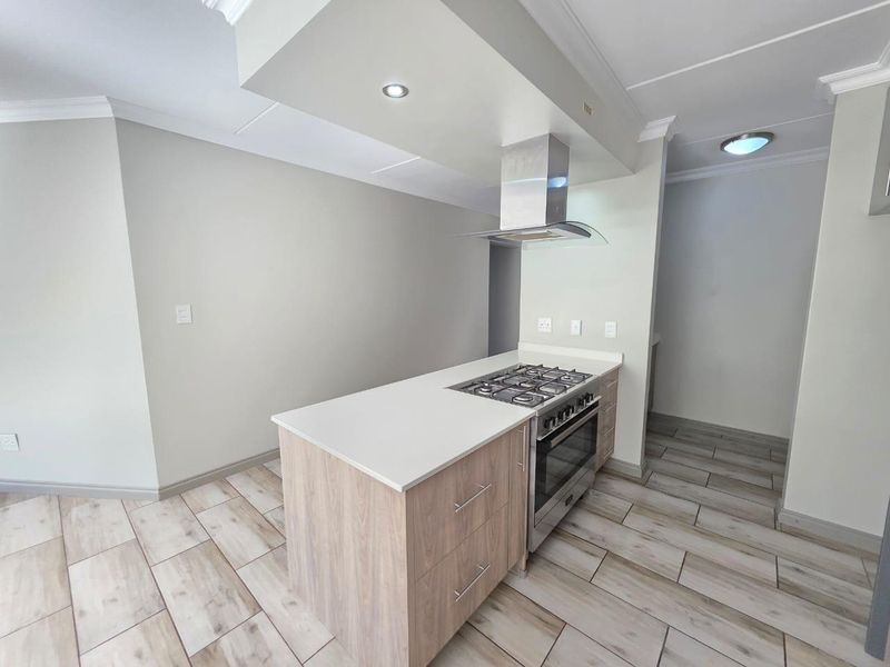 Modern kitchen featuring a central island with a gas hob, built-in oven, stainless steel extractor fan, and light wood cabinetry with stone countertops.
