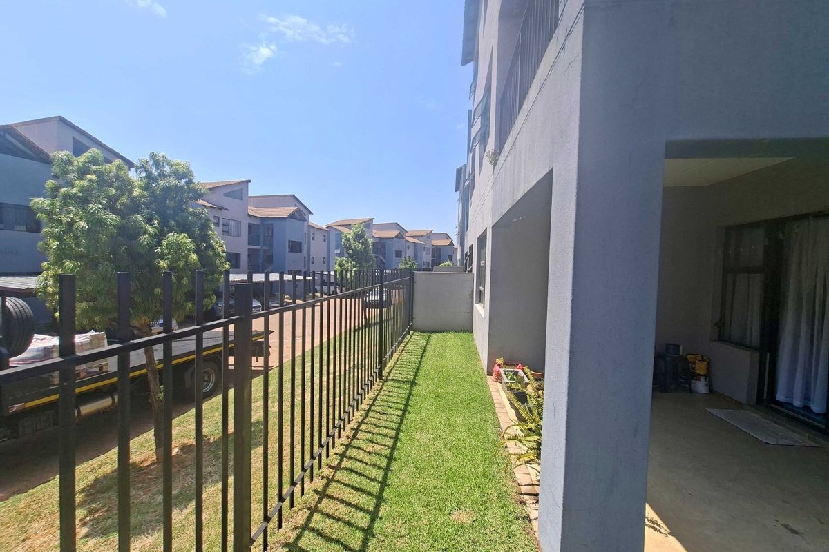 A ground floor apartment exterior featuring a private concrete patio, a small lawn area, and secure metal perimeter fencing.