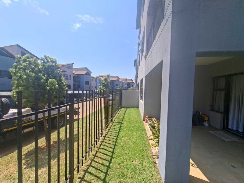 A ground floor apartment exterior featuring a private concrete patio, a small lawn area, and secure metal perimeter fencing.