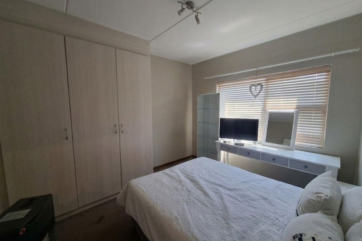 A functional bedroom featuring built-in wardrobes, a wall-mounted vanity unit, and venetian blinds, providing a neutral and practical living space.