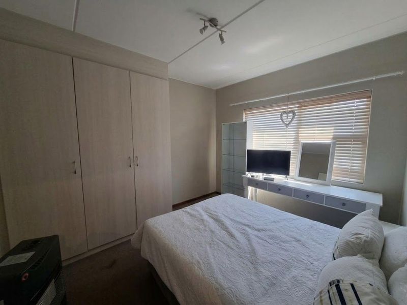 A functional bedroom featuring built-in wardrobes, a wall-mounted vanity unit, and venetian blinds, providing a neutral and practical living space.