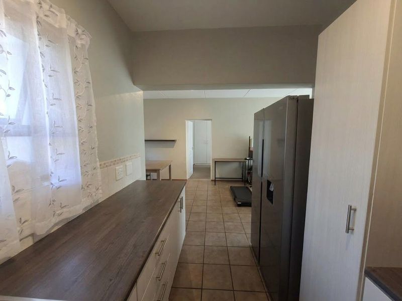 A functional kitchen area featuring laminate countertops, built-in cabinetry, and tiled flooring, leading into an adjacent living space.